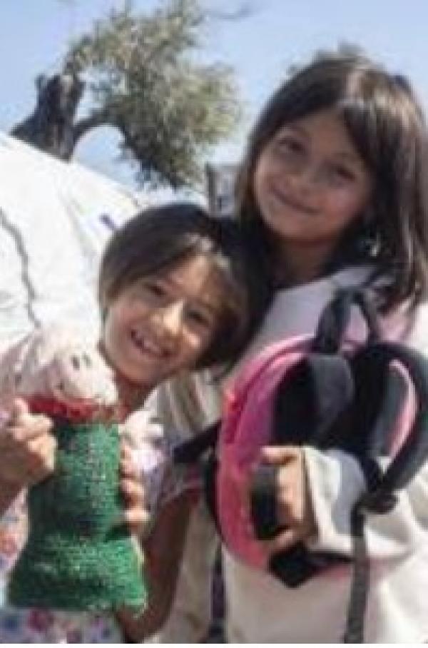 Two smiling children with a backpack and a doll